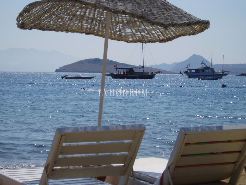 Straw parasols on Bitez beach, calm turquoise water and moored gulets