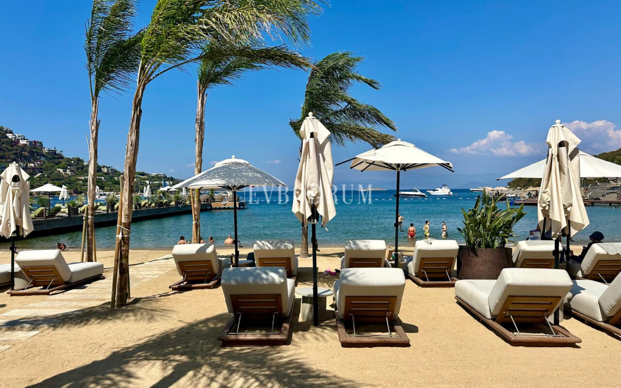 Ein Beachclub am Sandstrand in Türkbükü mit Liegen und Sonnenschirmen